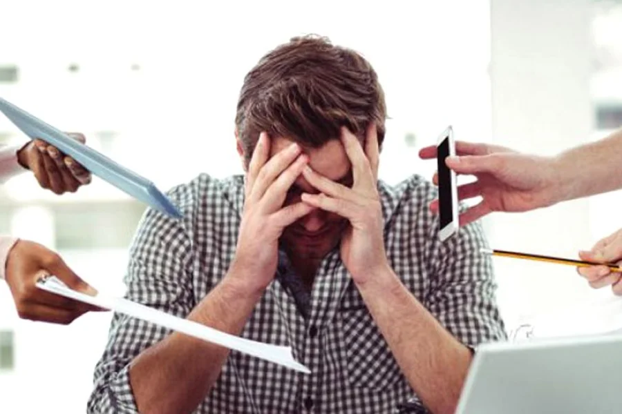 An executive with his head in his hands, surrounded by demands at his desk